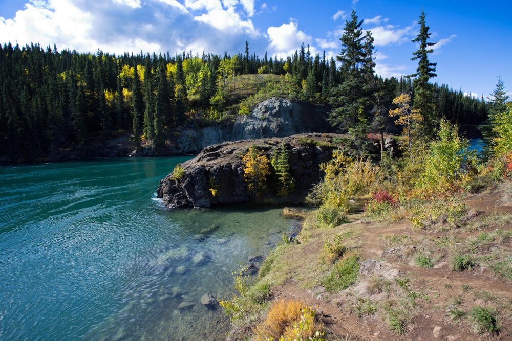 Brilliant turquoise water on the Yukon River, surrounded by rocks and green trees