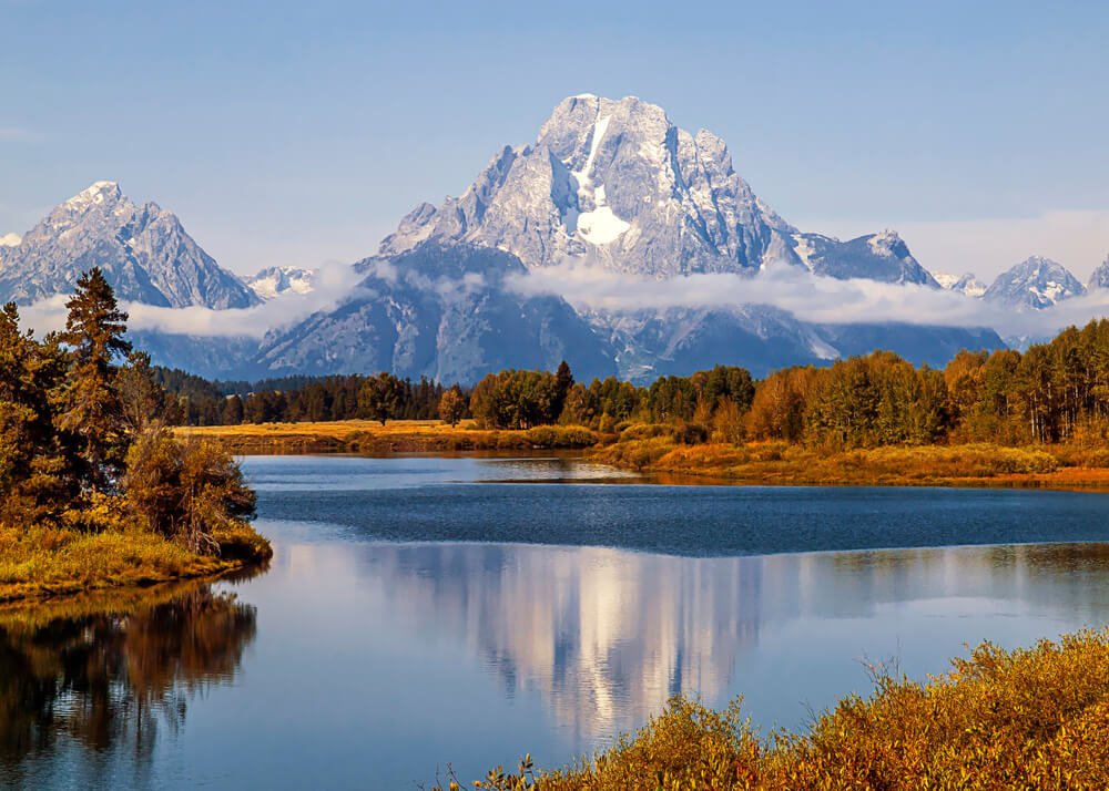 Mt. Moran at Oxbow Bend in Grand Teton National Park, reflected in the river which is surrounded by orange foliage in the autumn.