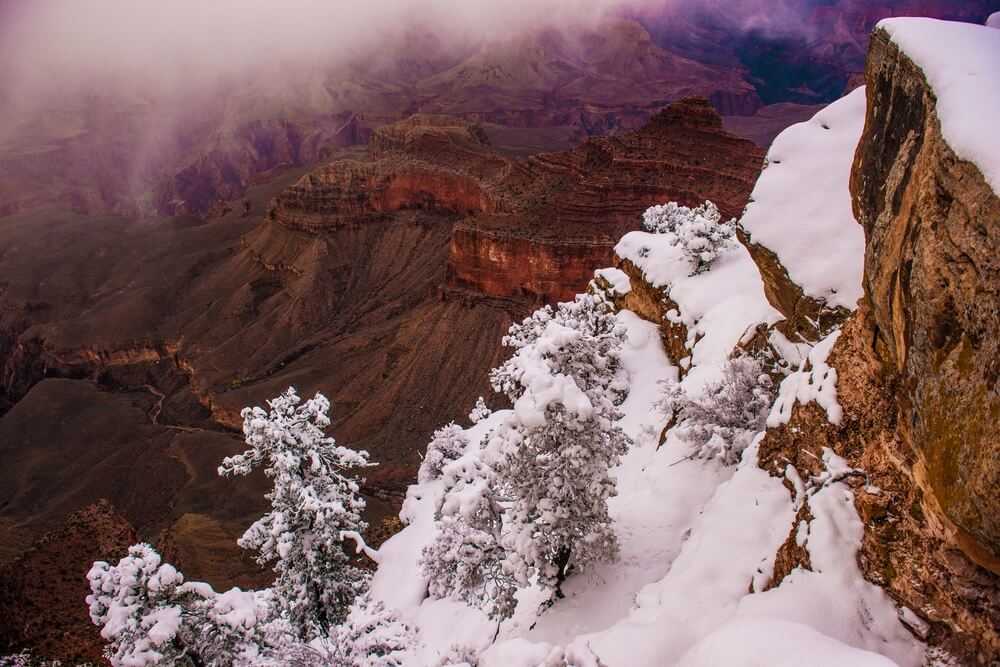 Snow covering red rocks at the Grand Canyon, other parts of the canyon left untouched by snow, as fog rolls on the top of the canyon 