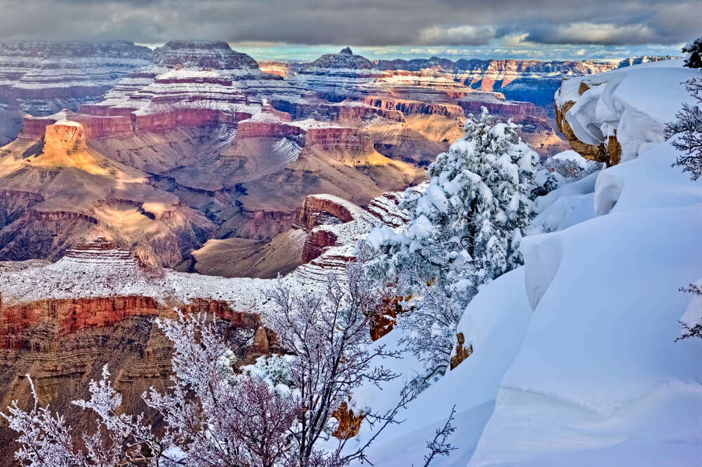 Winter landscape at the Grand Canyon, white snow blanketing the higher elevation pockets of the park and tops of the mesas, and the valley below showing red rock and orange rocks