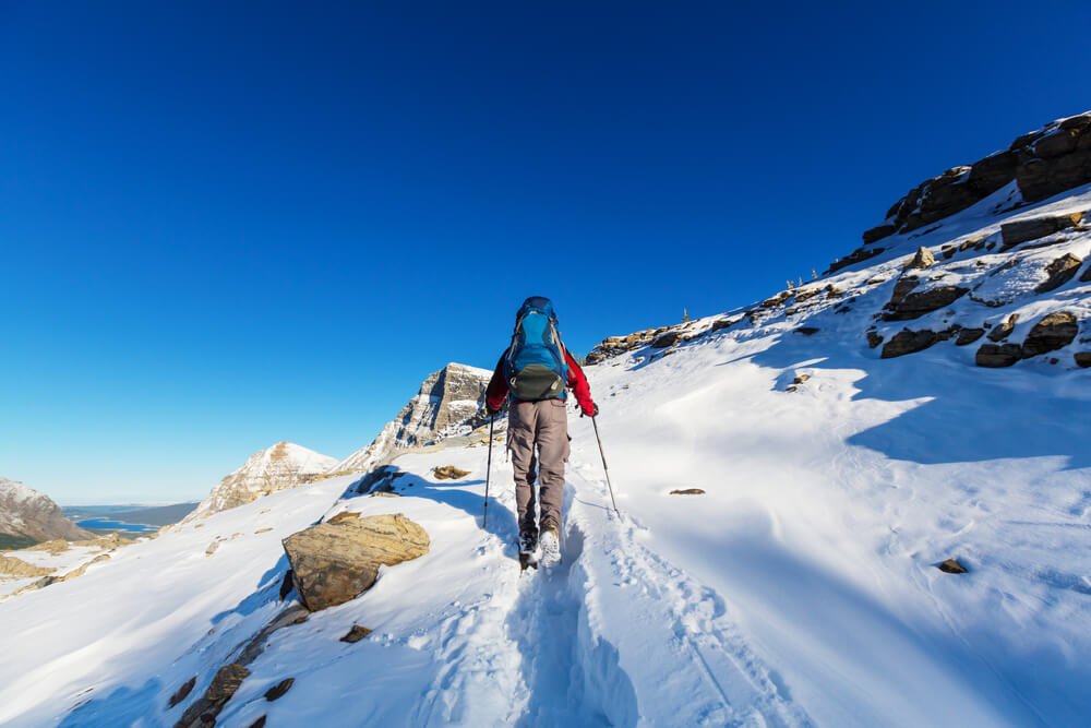 A man wearing weather-appropriate clothing hiking through the snow, exhibiting winter safety guidelines in Glacier National Park in the snow.