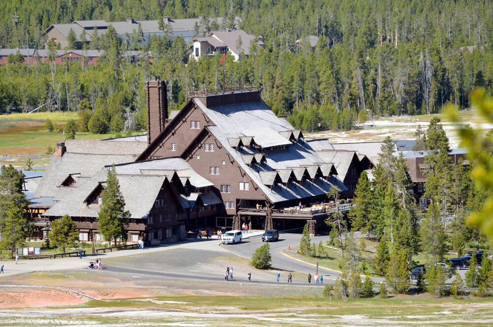 Old Faithful Lodge near the geyser, a large wooden mountain lodge surrounded by trees, a popular place to stay on a Yellowstone road trip