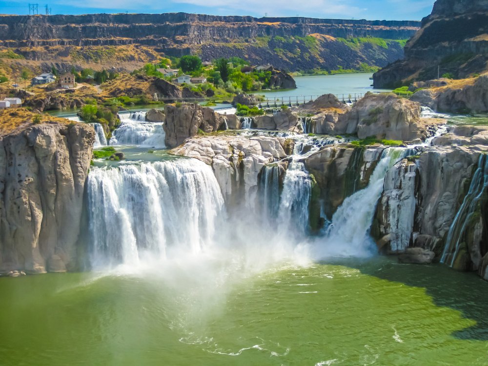 The waterfalls of Shoshone Falls cascading in a horseshoe shape over a large cliff edge, tumbling into a pale green pool of water below, surrounded by a rocky landscape.