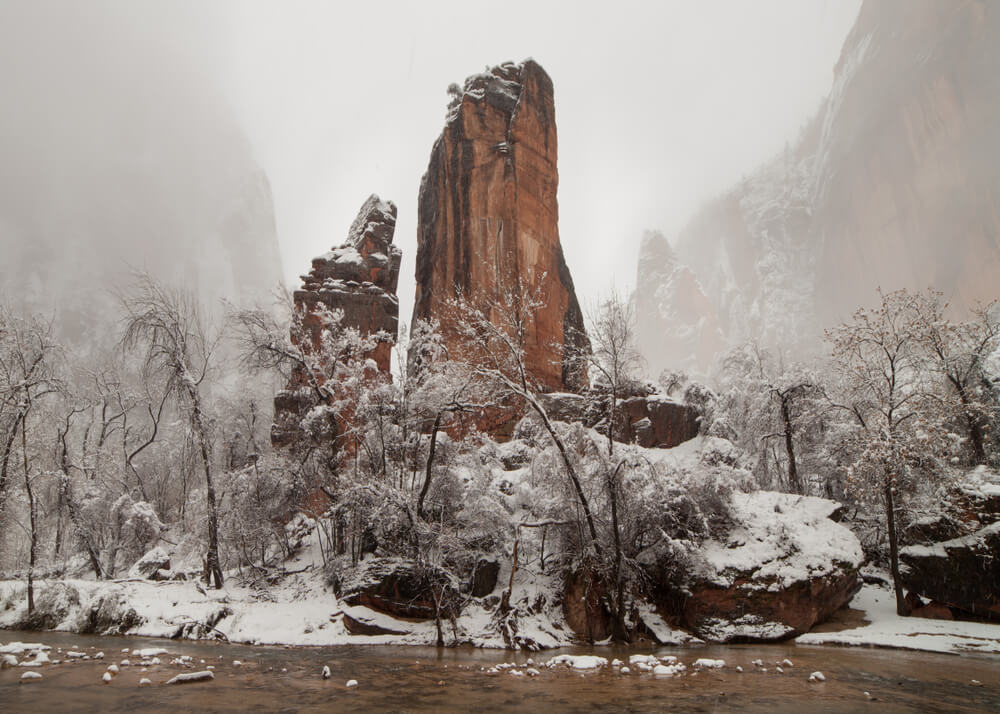 Rock formations covered in snow, surrounded by fog on a wintry day in Zion national park