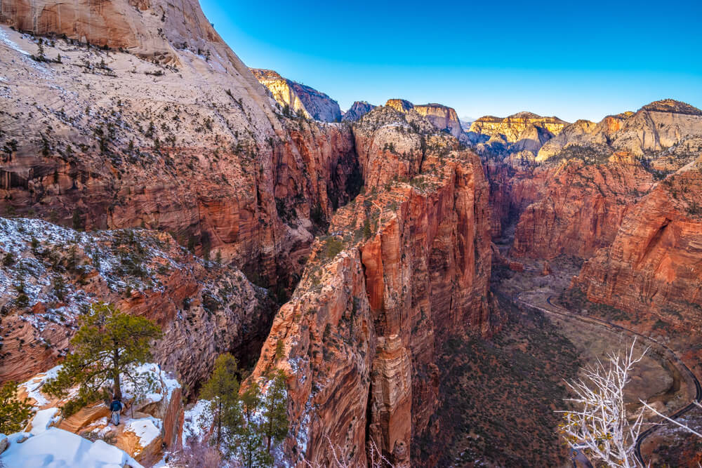 View of Zion's red rock cliff landscape juxtaposed with bits of white snow in the higher elevation crevices of the canyon on a blue sky winter day in Zion National Park