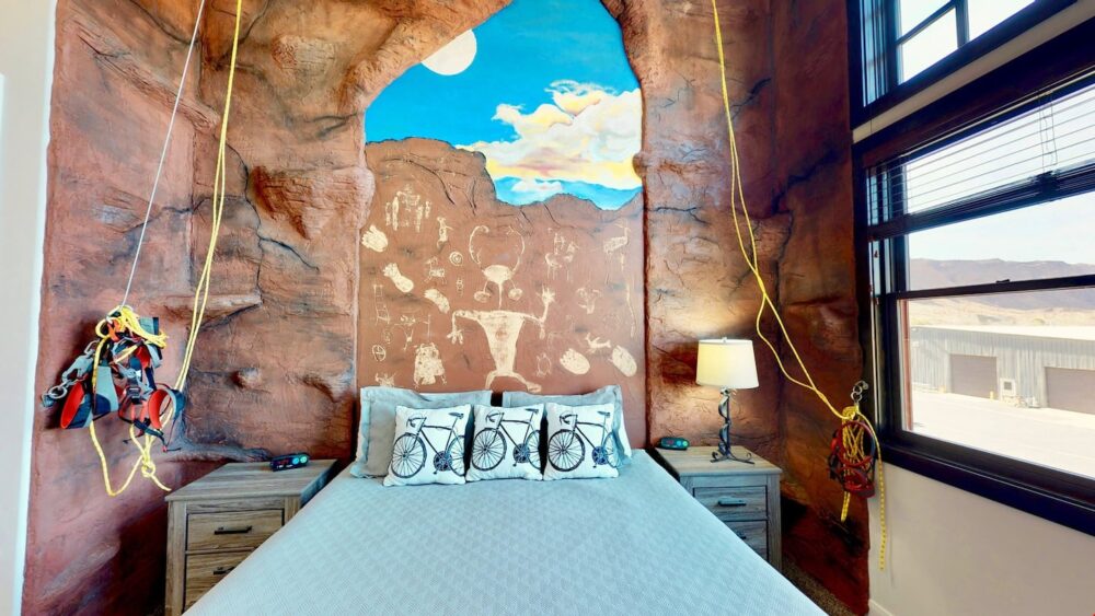 Unique Moab Airbnb concept: a bed with a wall at the headboard showing rock paintings, with rock climbing gear and notches in the wall to try out rock climbing on.