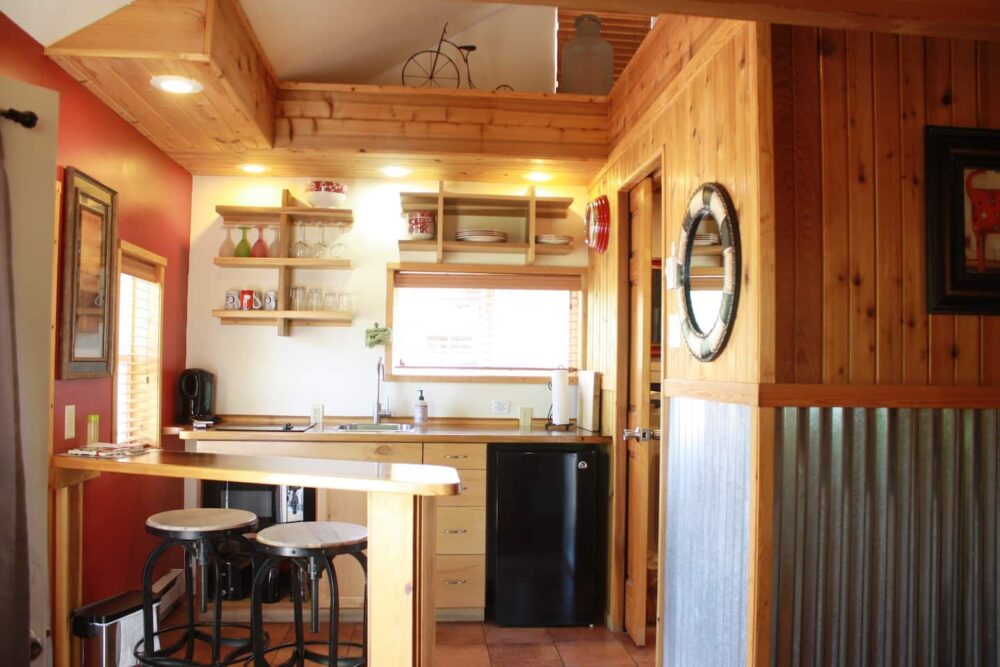Wooden house with aluminum wall paneling up to halfway up the wall, showing an open layout kitchen with two stools for eating at the bar.