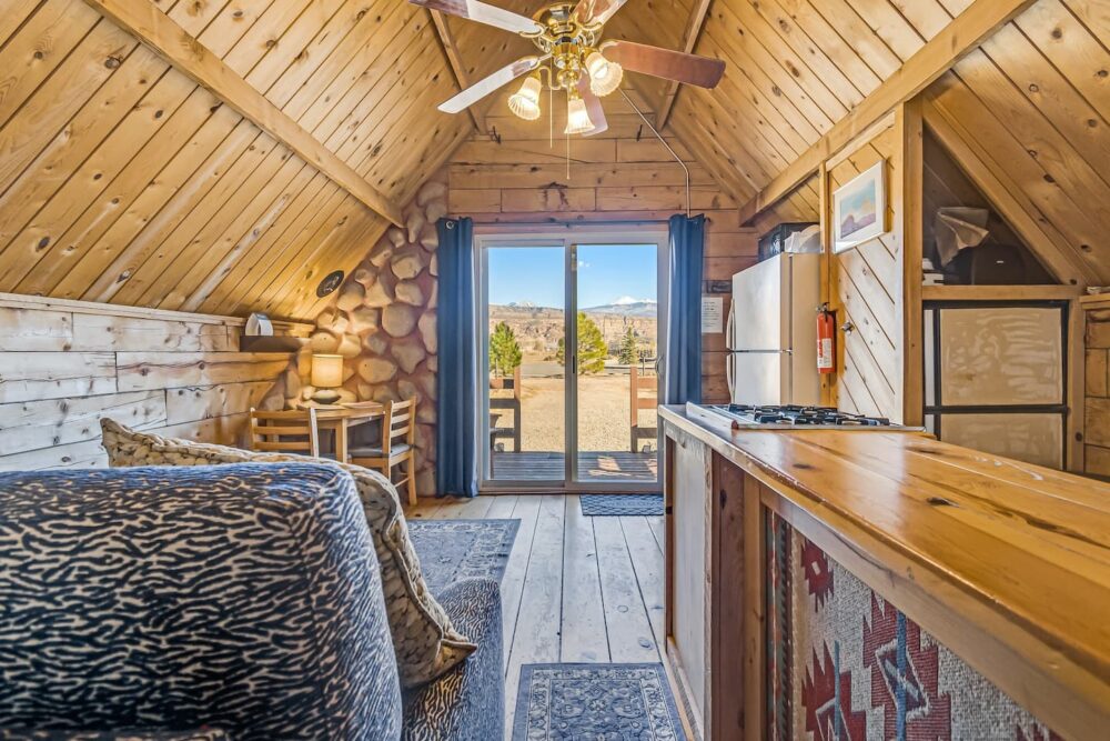 Interior of a rustic A-frame cabin with light wood ceilings, glass doors opening up into the Moab landscape.