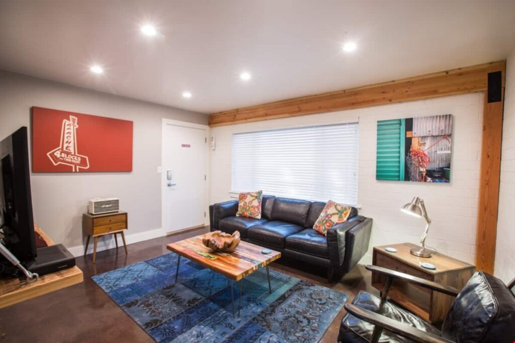 Black leather sofa, rug, coffee table, two paintings on the wall in a modern style, and a little white vintage radio on a mid-century modern drawer.