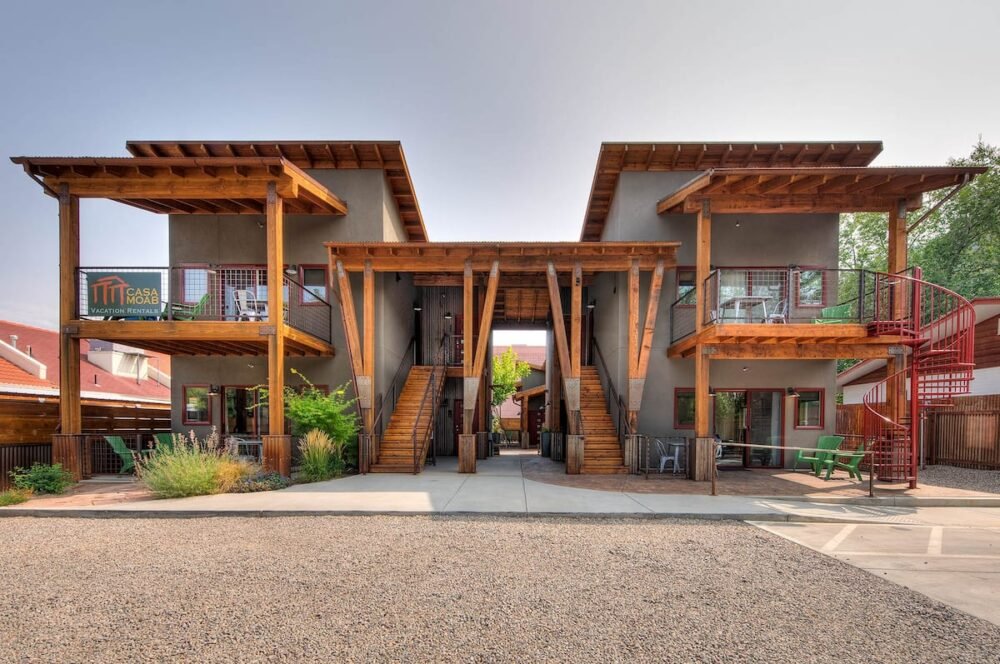 Two gray and wooden houses connected by a roof and twin staircases leading up the upper level, with gravel on the ground in front of the houses, at this popular Airbnb in Moab.