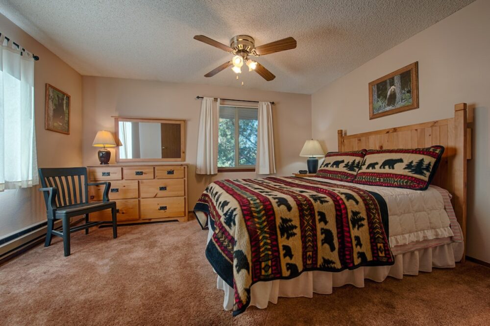 Bed with a cozy red and white and black blanket on top of it with carpet and a ceiling fan.