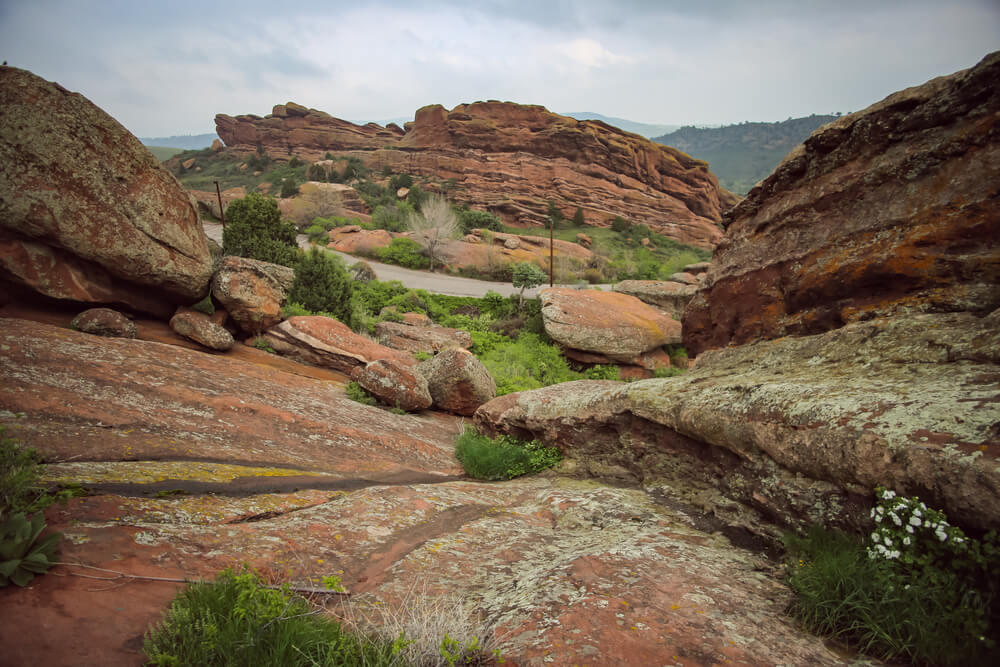 Red rock covered in a green mossy sheen, with hiking path visible in the distance, on a hike near Denver
