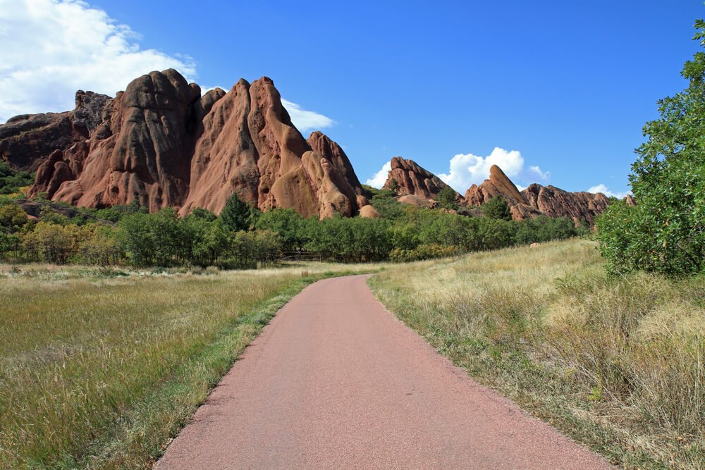 Paved path with sandstone orange rock formations forming peaks in the sky