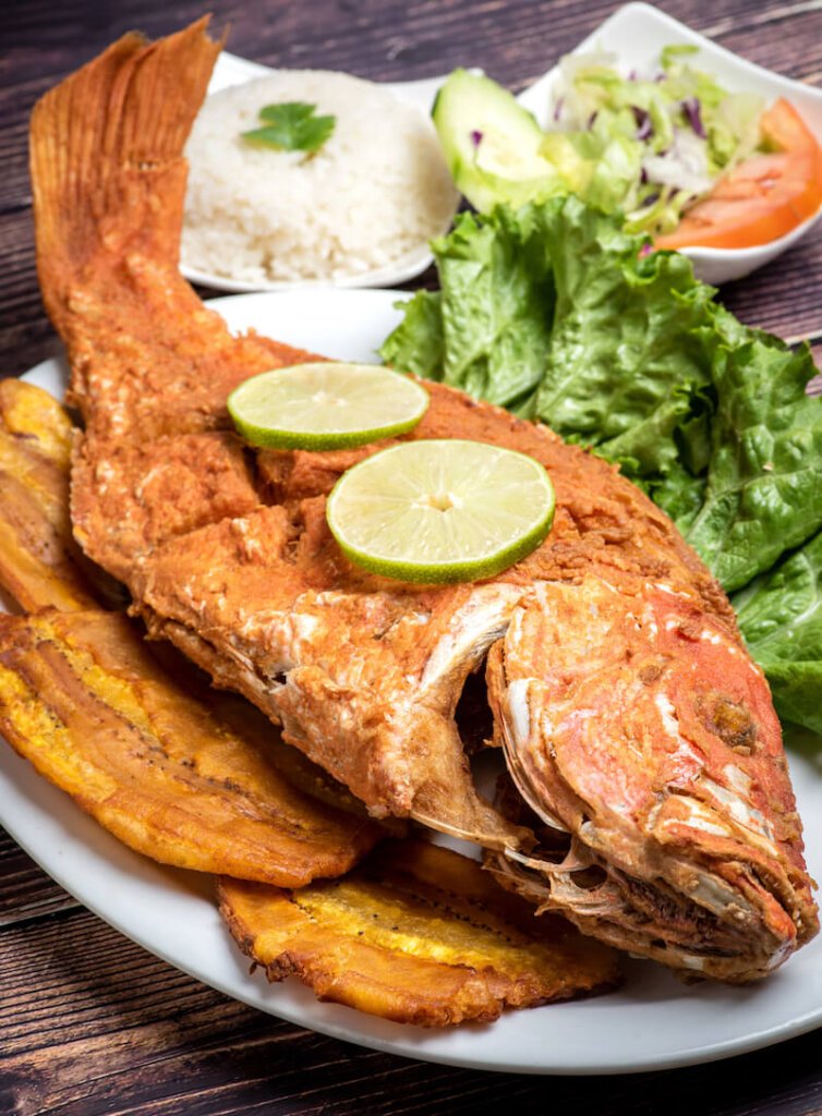 a fried red fish with flattened fried plantains