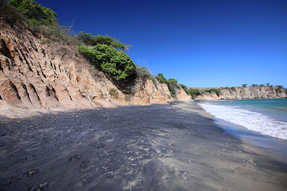 Black sand beach next to a cliff in Puerto Rico with beach water and ocean waves