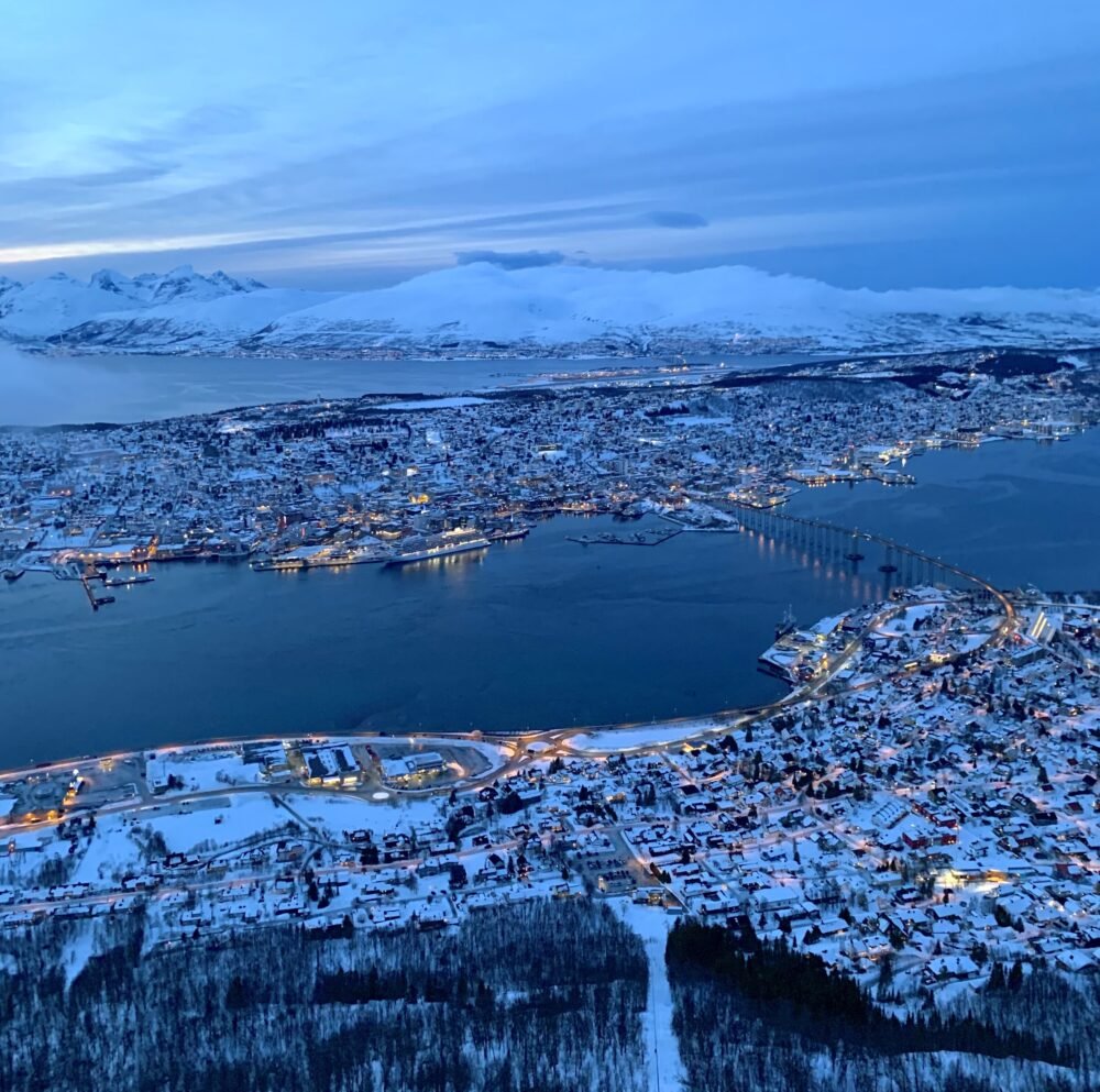 view from the top of tromso's cable car of tromso at night with all the city starting to light up below you