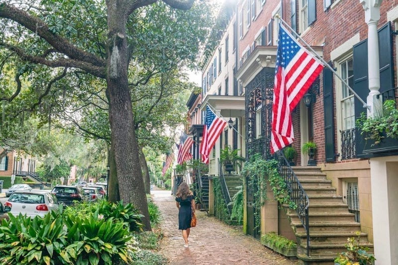 american flags, beautiful brick houses, and oak trees and one woman walking down the street in savannah ga