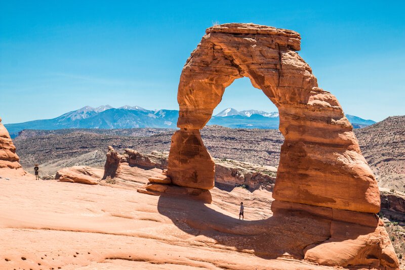 man standing below delicate arch in utah wearing hiking boots