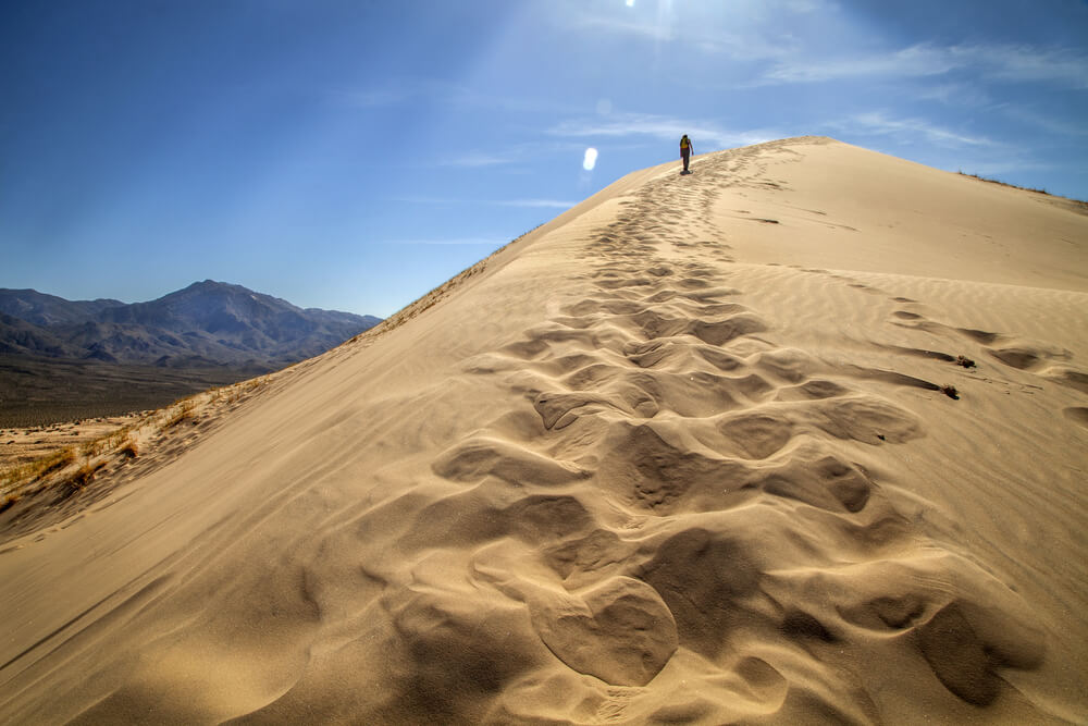 trail of footprints left in the sand as a single hiker ascends the sand dune