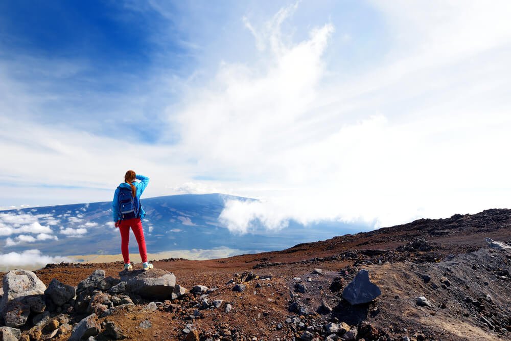 female hiker standing on mauna loa looking at the clouds and views below the summit