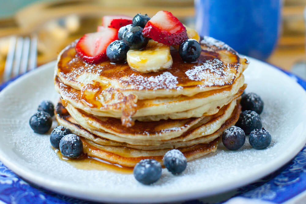 A stack of many pancakes with blueberries, strawberries and bananas.