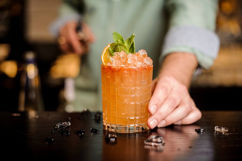 Man's hand serving an orange drink with crushed ice and mint