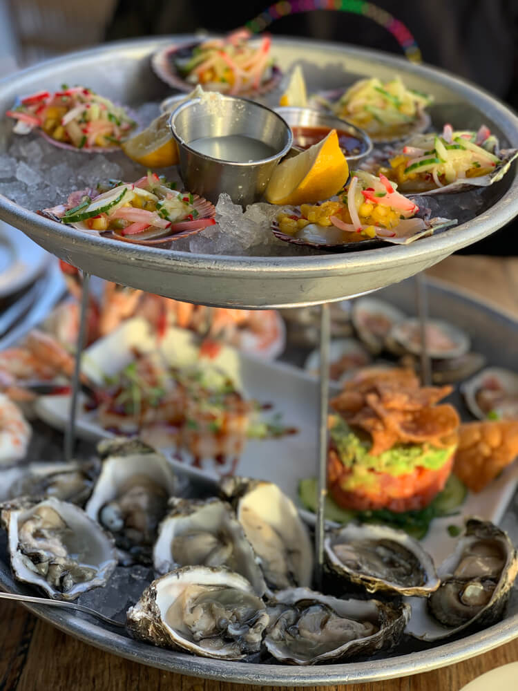 Platter full of fresh seafood including oysters, clams with a salsa on top, and poke