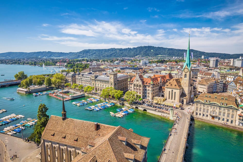 aerial view from one of the churches of zurich looking over the water and the old town of zurich and its bridges on a sunny day with a few clouds
