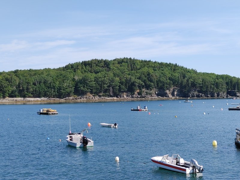 boats in the water of maine's bar harbor with an island in the distance