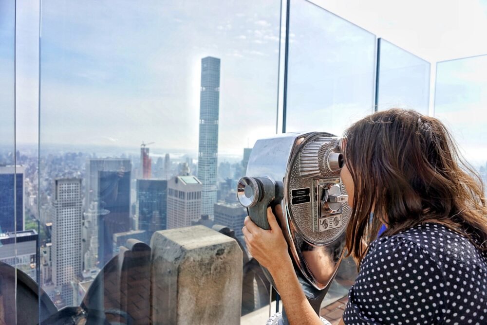 Allison Green smiling as she looks through a viewfinder at buildings in NYC