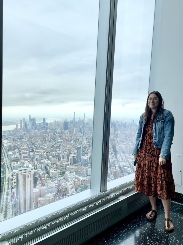 Allison Green smiling at One World Observatory wearing an orange dress and jean jacket and sandals