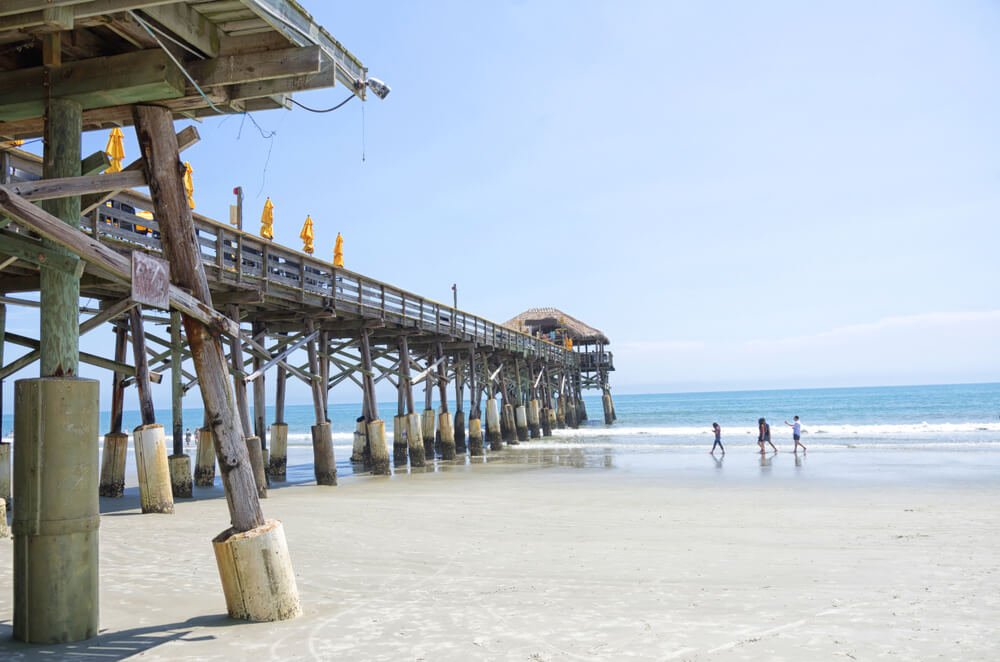 pier in cocoa beach florida with three people walking on the beach sand