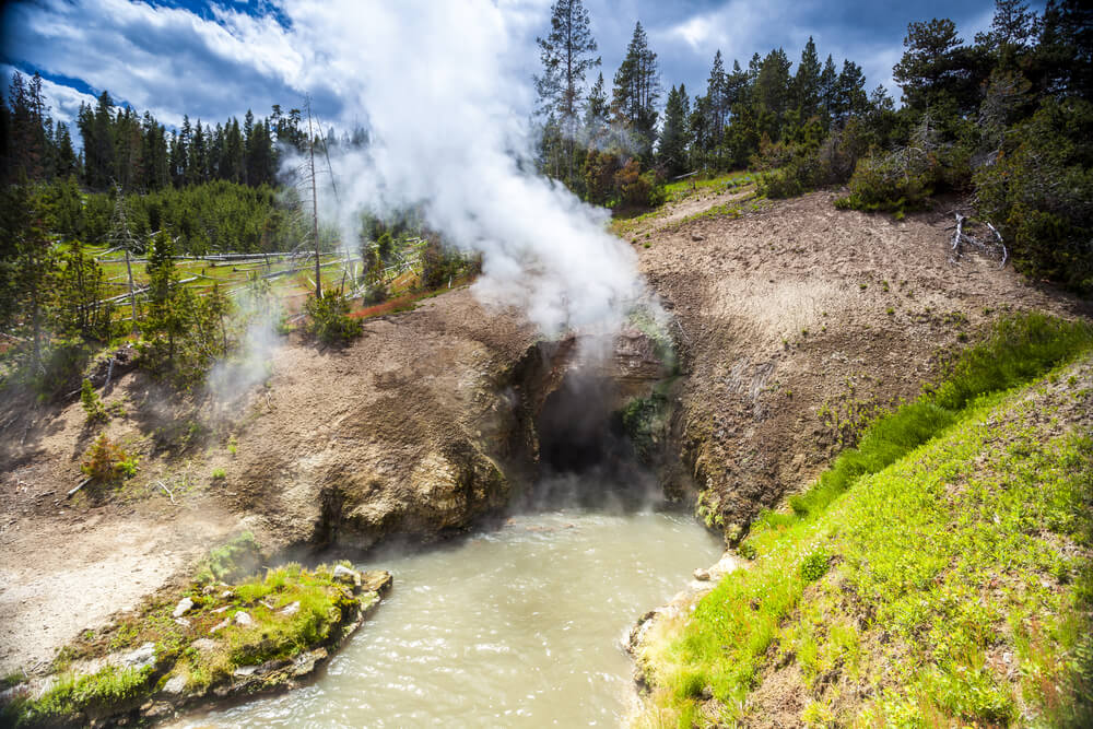 Bubbling mud pool in Yellowstone National Park with steam rising off the top at the Dragon's Mouth part of the loop