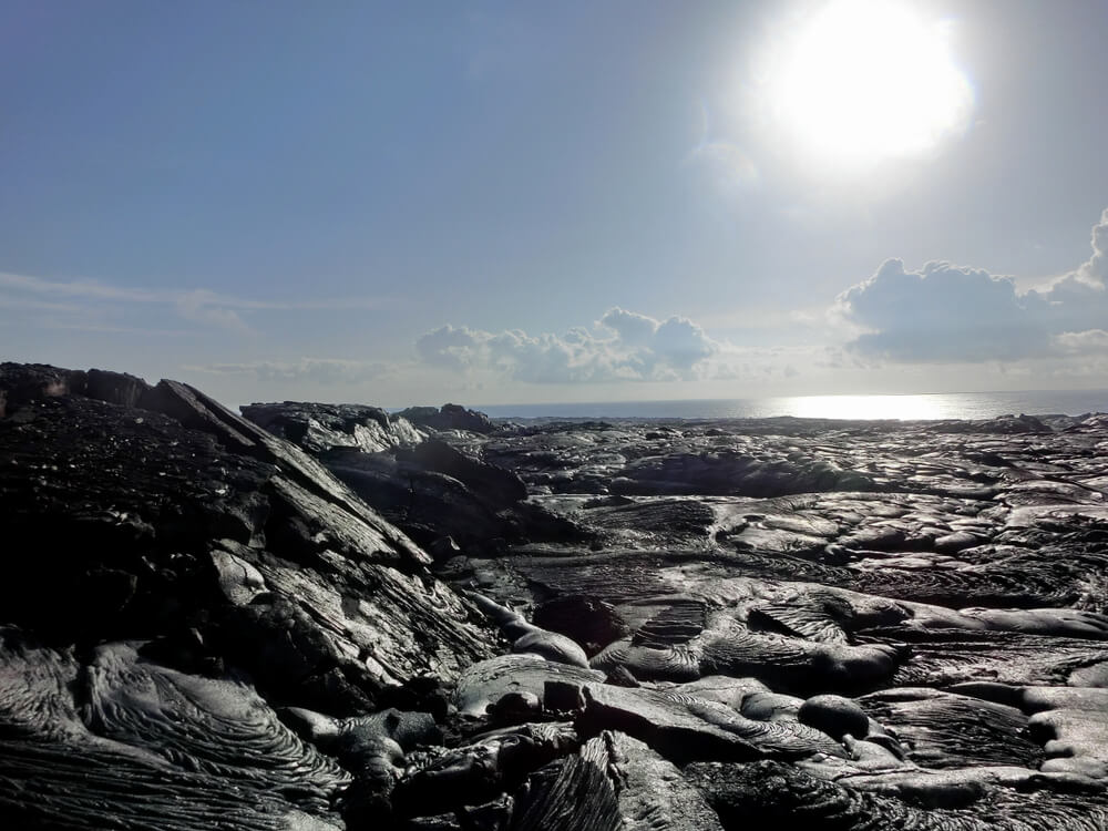 Lava field of Hawaii, crossing a black rock barren wasteland, with Pacific Ocean in the distance
