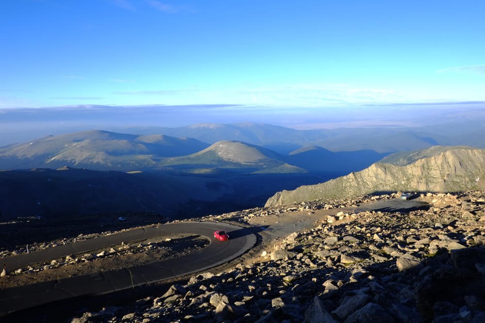 Red car going up a mountain pass on a sunny day with hills and mountains in the background