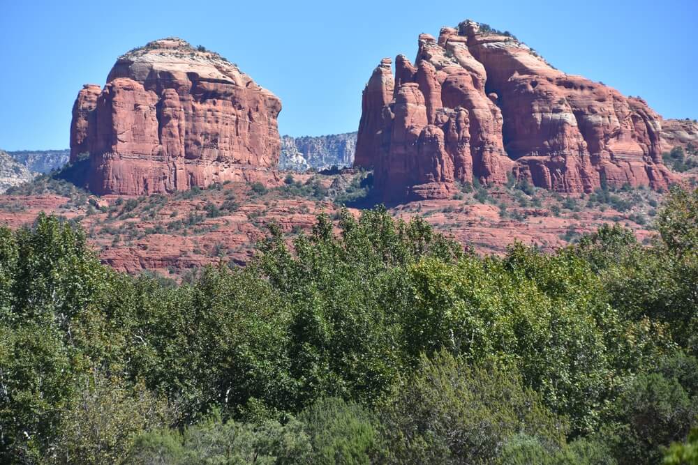 red rock formations of sedona with green trees in the foreground and two towering formations in the distance