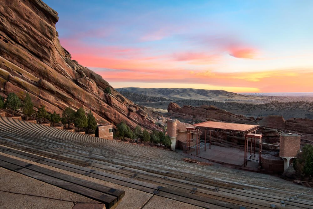 Red rocks amphitheater at sunrise with colors over the horizon illuminating the red rock and stadium steps