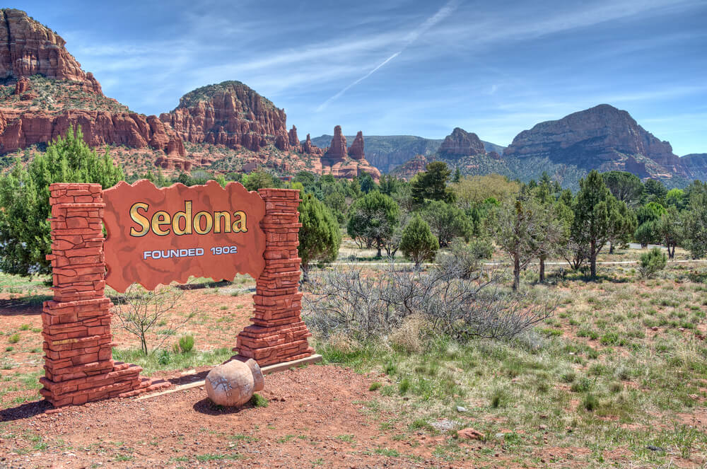 Sign that reads "Sedona founded 1902" with red rock formations and trees in the foreground of the photo