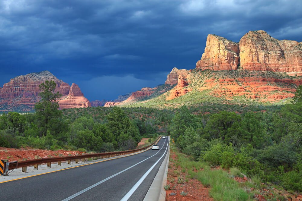 Cloudy sky over scenic view of the Bell Rock from the highway near Sedona, two cars on the road in the distance.
