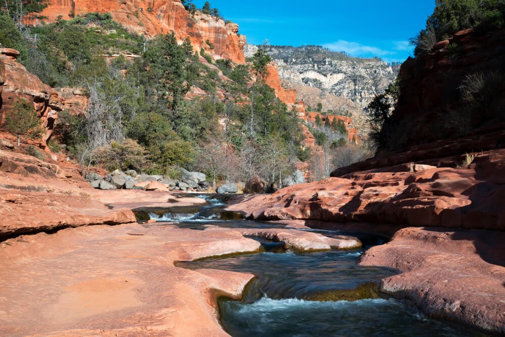 The natural "water slide" of Slide Rock State Park with mountains around it and cool water running through Oak Creek