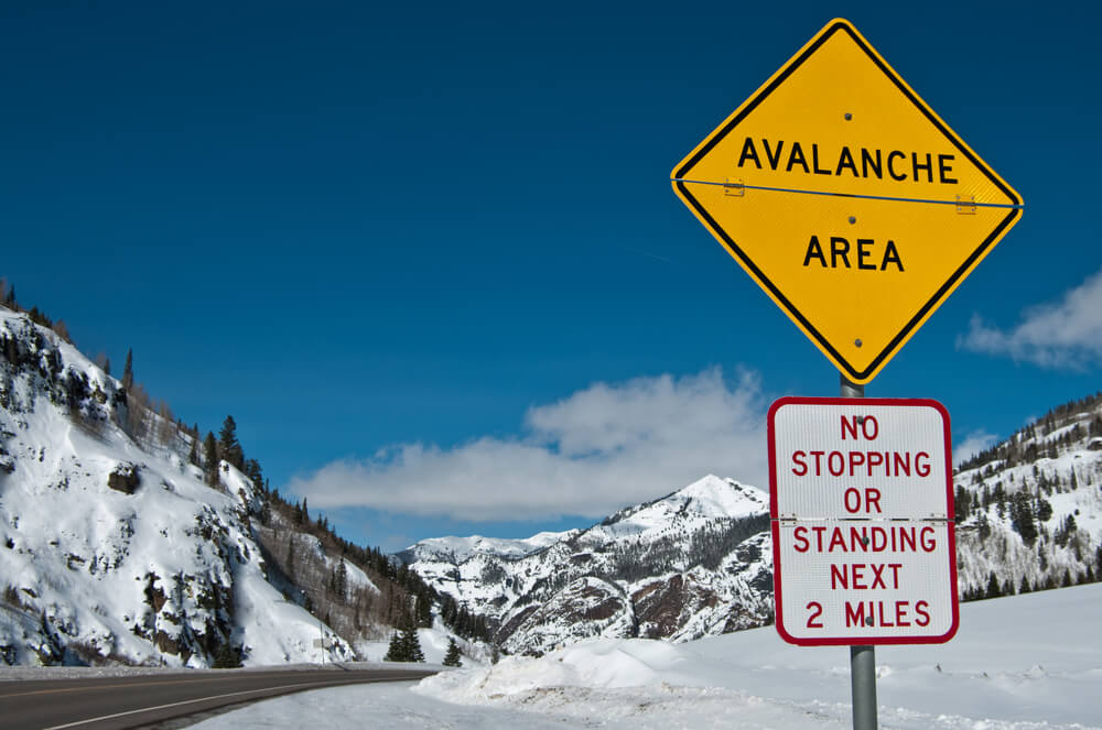 Sign reading "avalanche area: no stopping or standing next two miles" with snow in the background