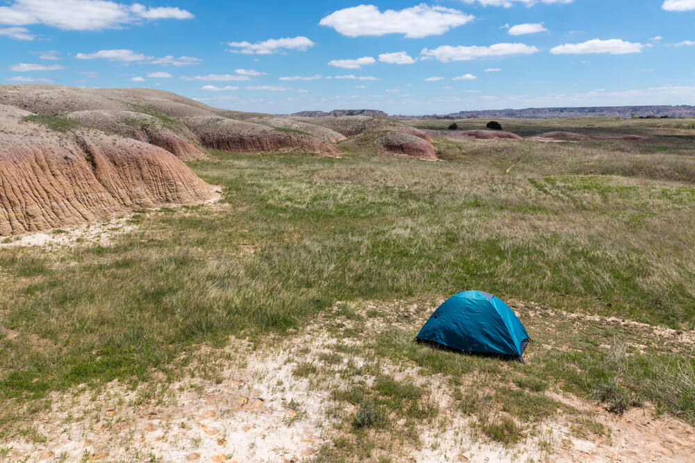 Blue tent contrasting against the red rock and green grass landscape of Badlands National Park