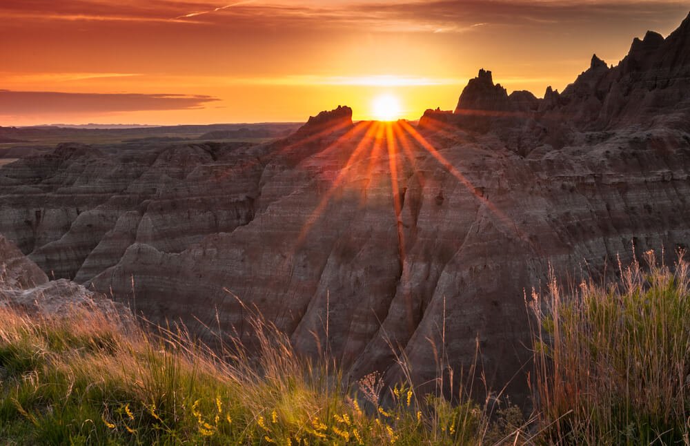 Sunset over the Badlands of South Dakota with a sunburst effect and grass in the foreground