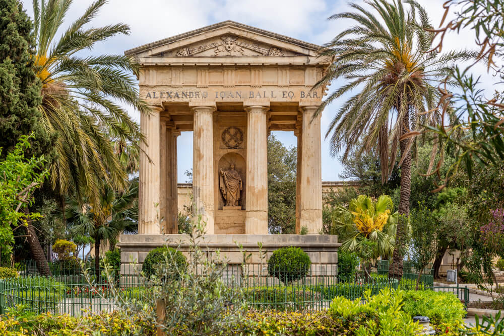 A view of a building with four pillars in Lower Barrakka Gardens surrounded by palm trees and plant life.