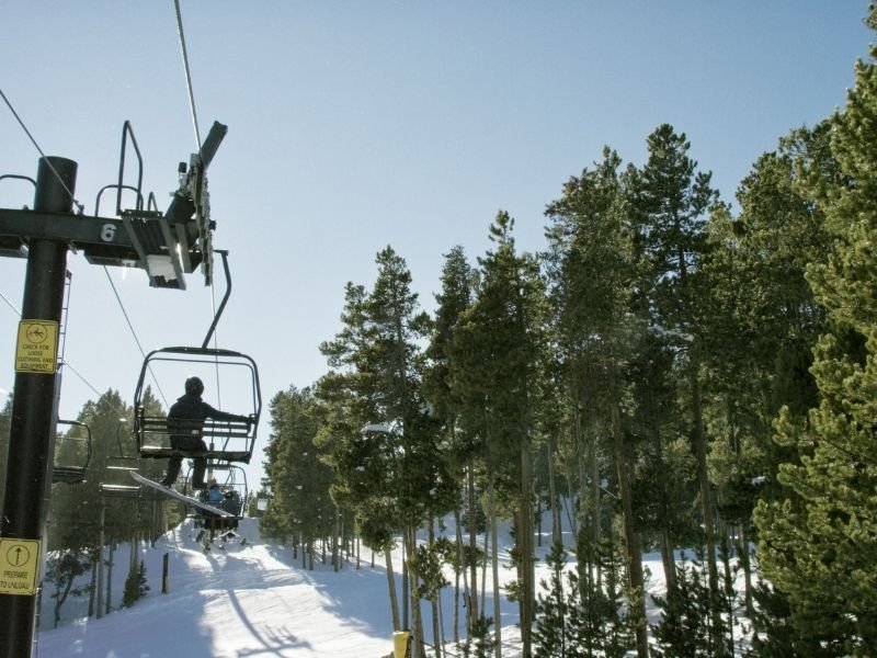 a man with a snowboard taking the chairlift up to eldora mountain resort, near boulder colorado in winter