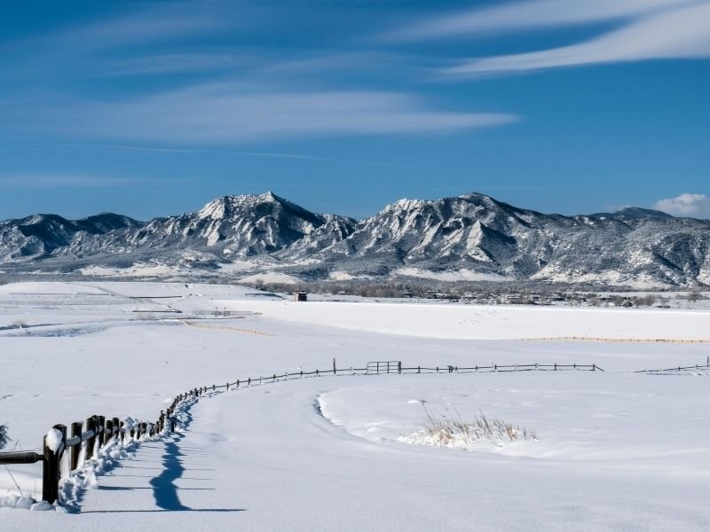 a snowy landscape in front of the flatirons section of the rocky mountains of colorado in boulder in winter