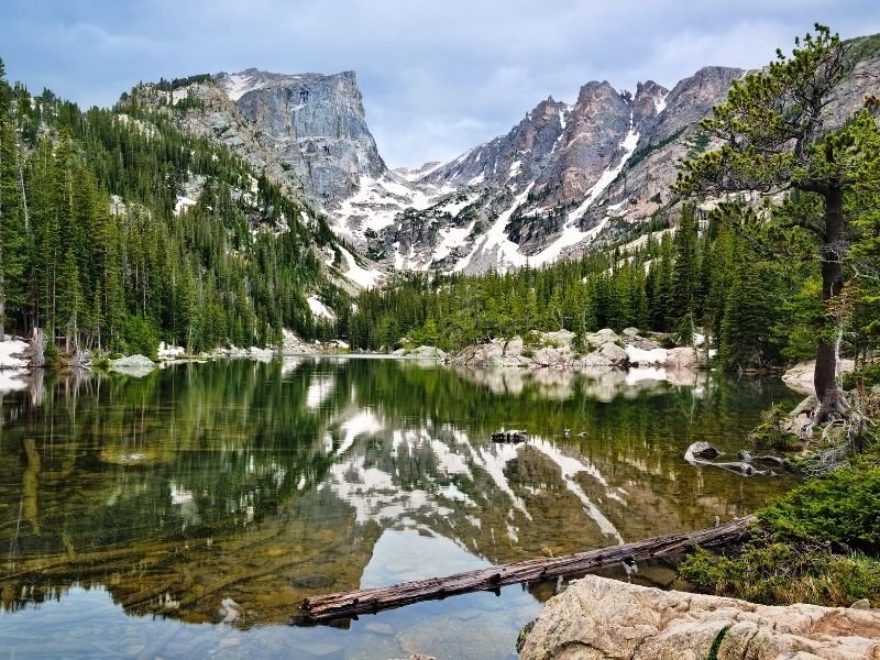 Hiking in Rocky Mountain National Park at the beautiful Dream Lake with still, glassy water reflecting trees and snow-dotted mountain peaks