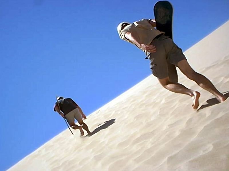 people sandboarding and walking up a sand dune