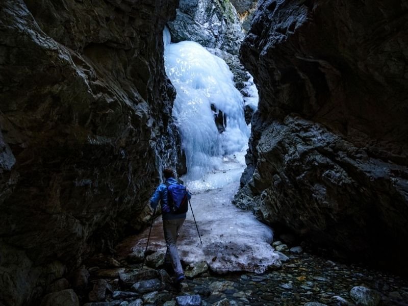 man hiking to a frozen waterfall in a canyon