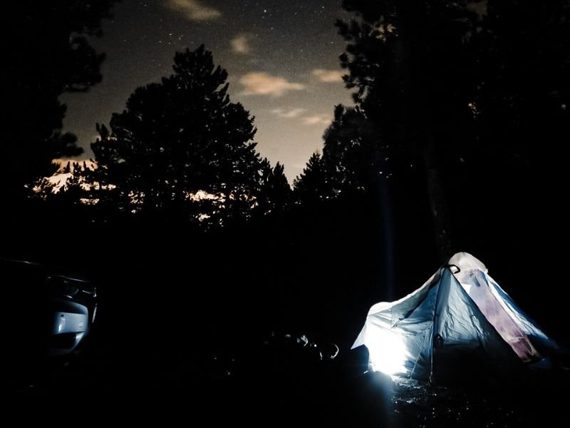 Camping tent in Colorado lit up from within with stars above in the sky